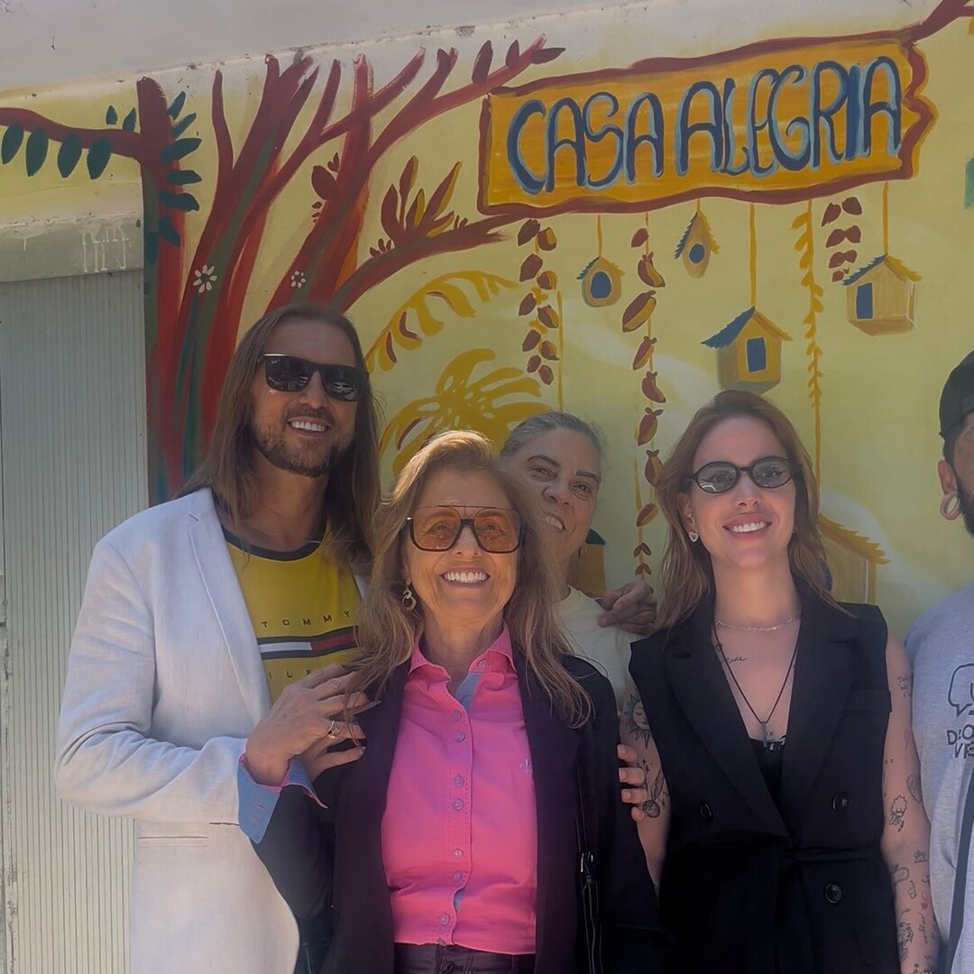 Grupo de pessoas diante de um mural colorido com a identificação Casa Alegria.